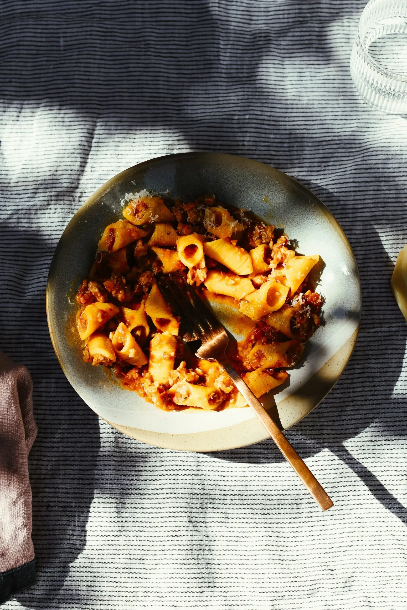 A close up photo of a plate of spicy sausage ragu served with fresh garganelli pasta, pictured in dappled sunlight. 