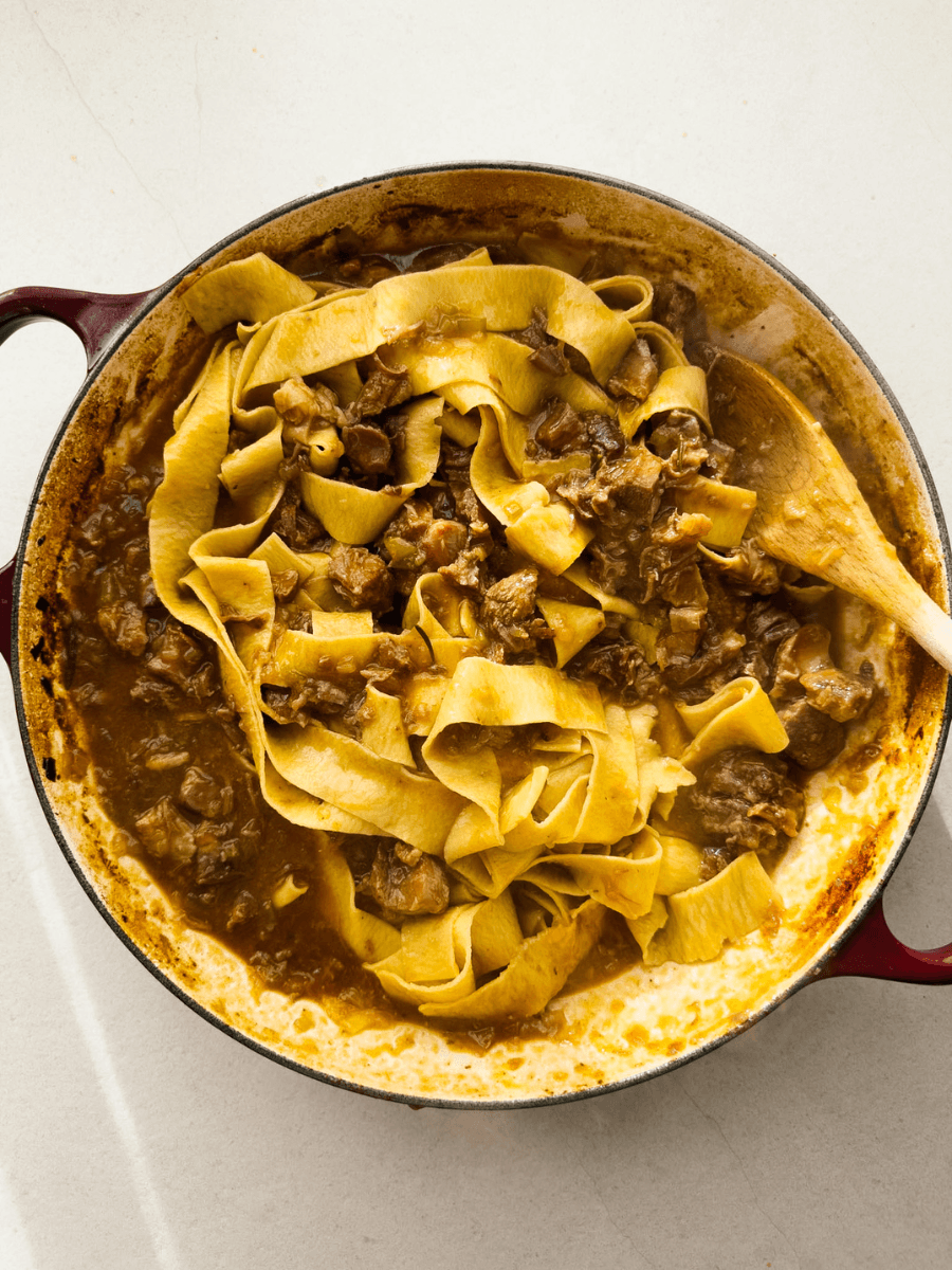 A top-down view of a shallow casserole containing fresh pasta with a rich meat sauce. 