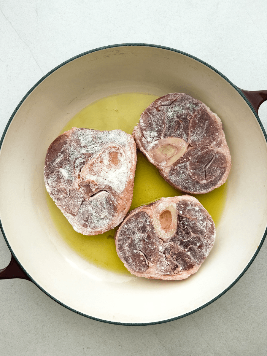 Raw ossobuco pieces are lightly coated in flour and seared in olive oil, in large, heavy-based pan. 