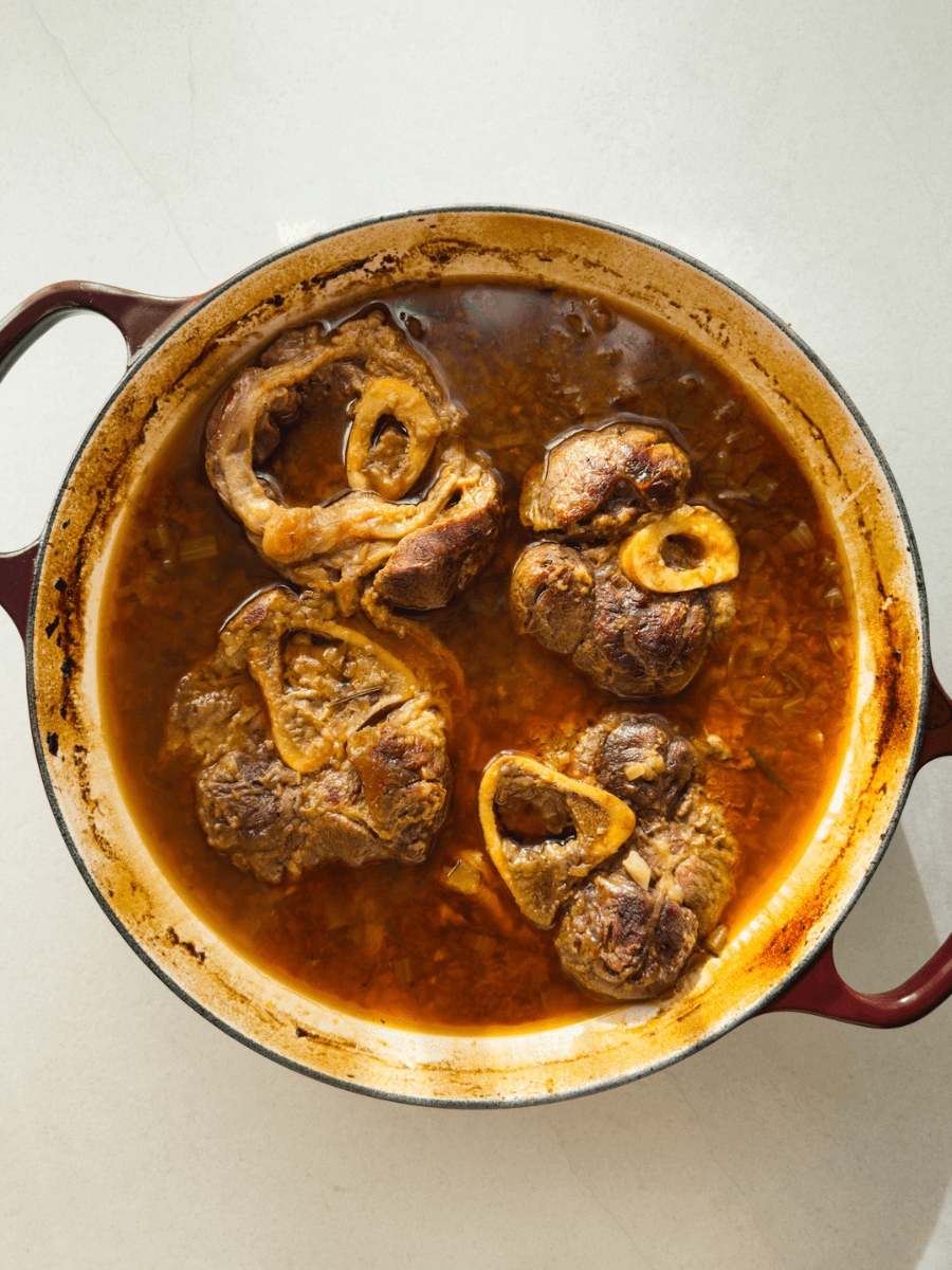 A top-down photo of slow-cooked ossobuco pieces, in a reduced braining liquid. 