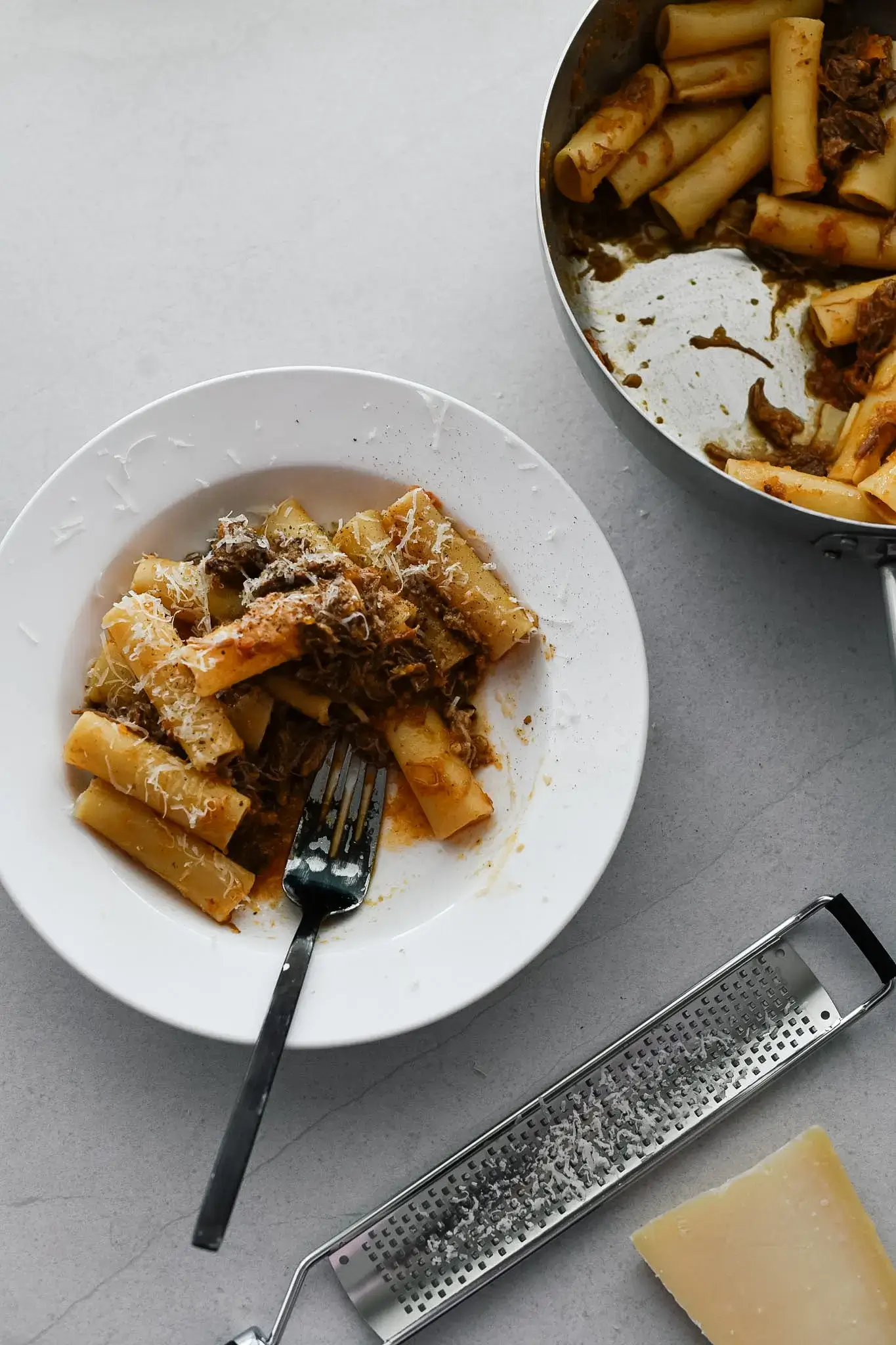 A top down photo of a white bowl with beef short rib ragu and a large tube pasta. 