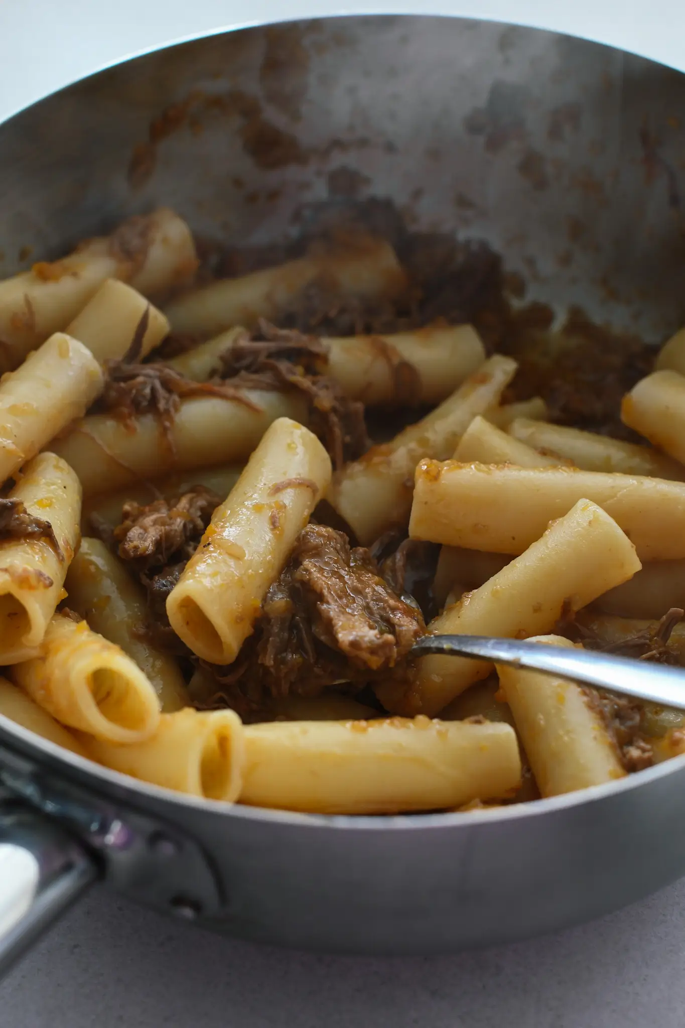 A close up photo of a pan of pasta with a luscious short rib ragu. 