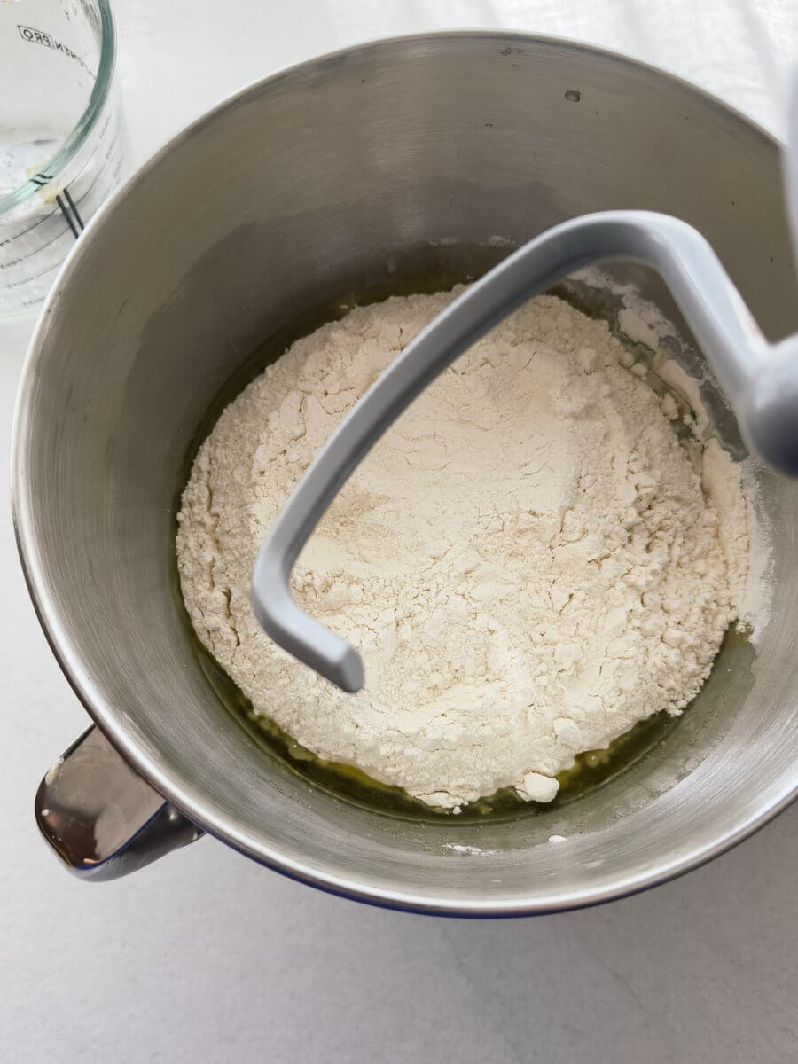 Ingredients for an easy overnight pizza dough are shown in the bowl of a stand mixer fitted with a dough hook. 