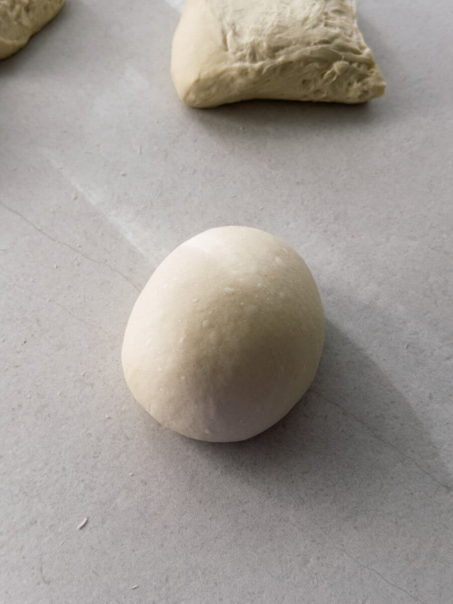 A close up photo of a preshaped pizza dough ball ready for cold fermentation. Visible air pockets are in the dough.  