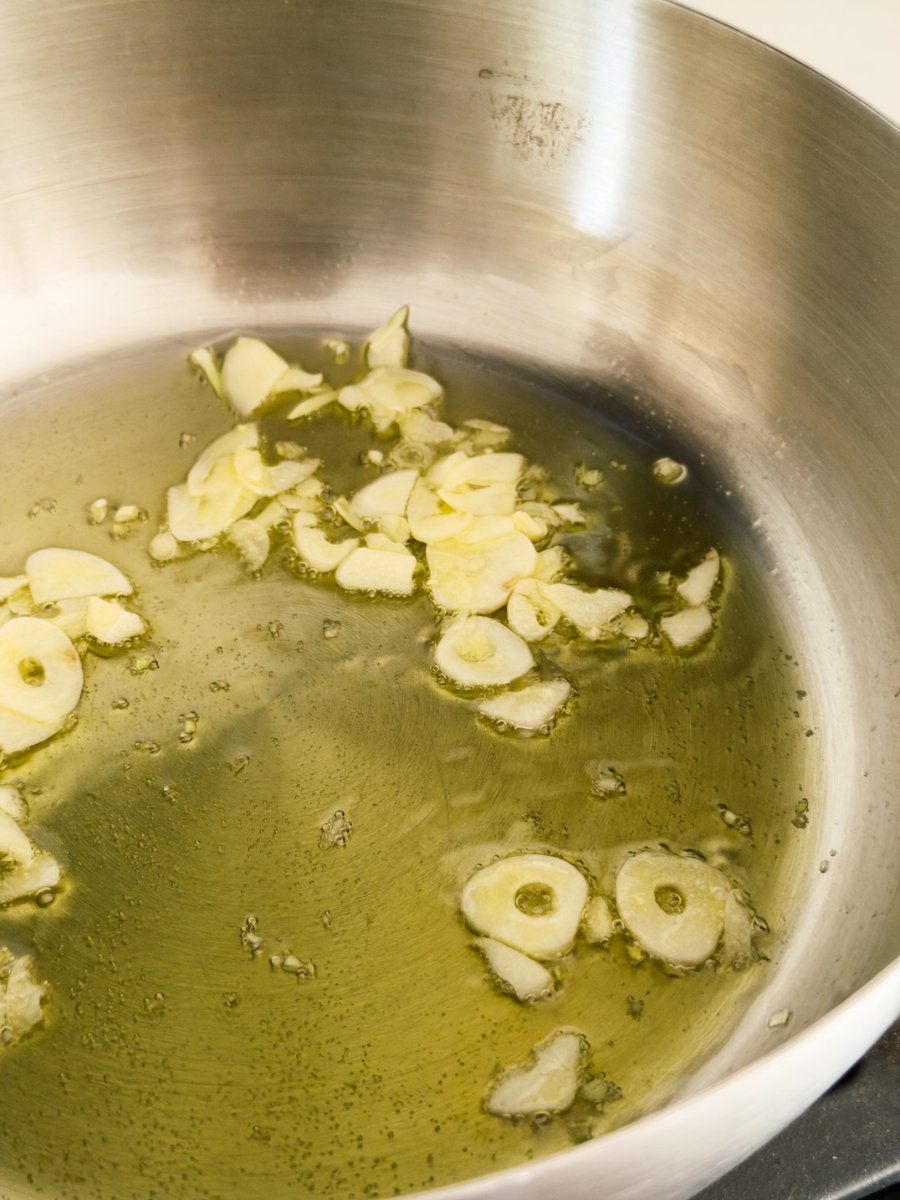 Thinly sliced garlic sizzles in olive oil in a stainless steel pan. 