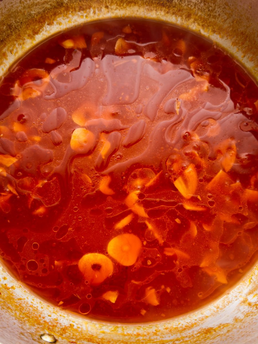 A top down photo of a red past sauce, with slices of garlic visible, before it is reduced down. 