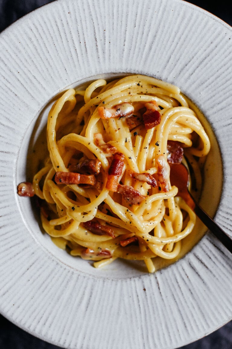A close up, top down photo of a plate of authentic spaghetti carbonara, made with eggs, pecorino romano and crispy guanciale.