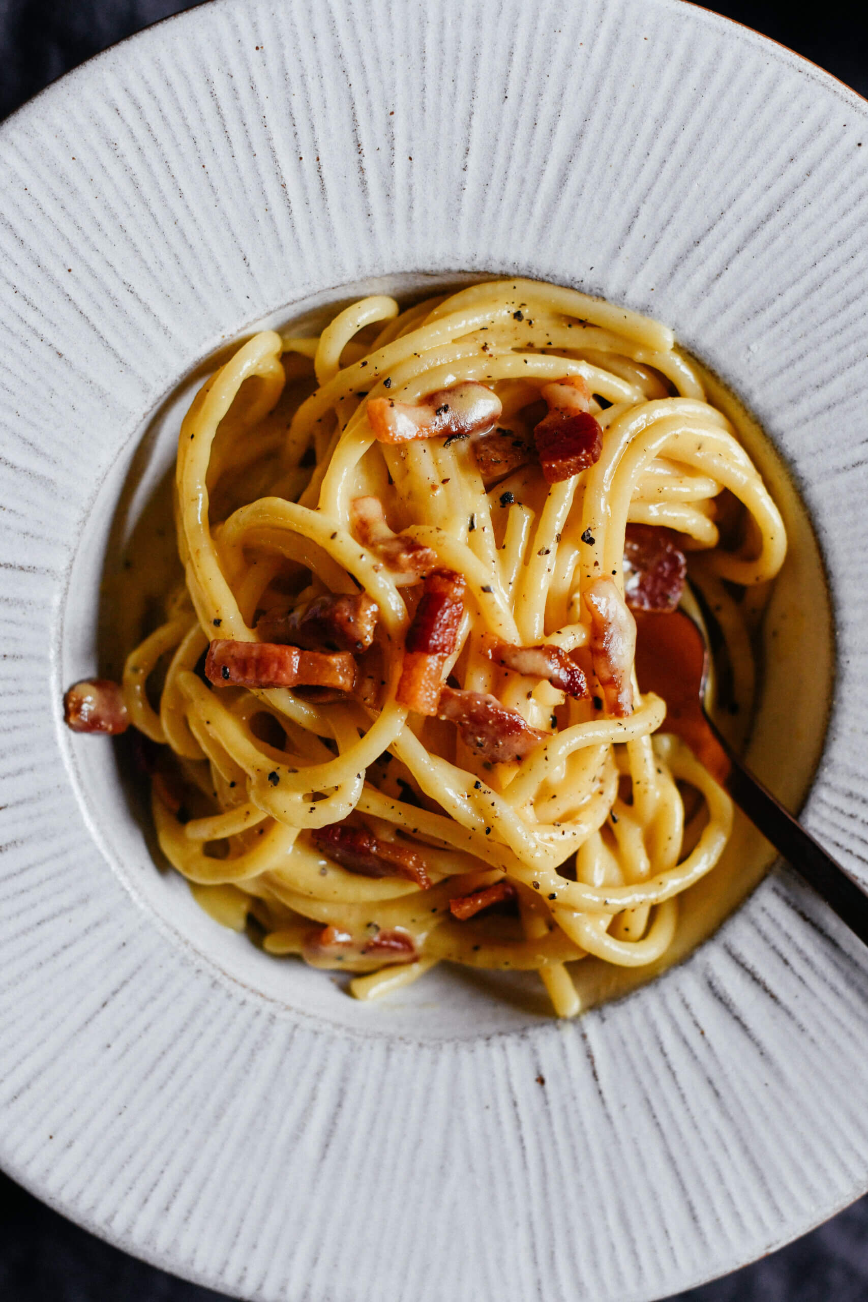 A close up, top down photo of a plate of authentic spaghetti carbonara, made with eggs, pecorino romano and crispy guanciale.