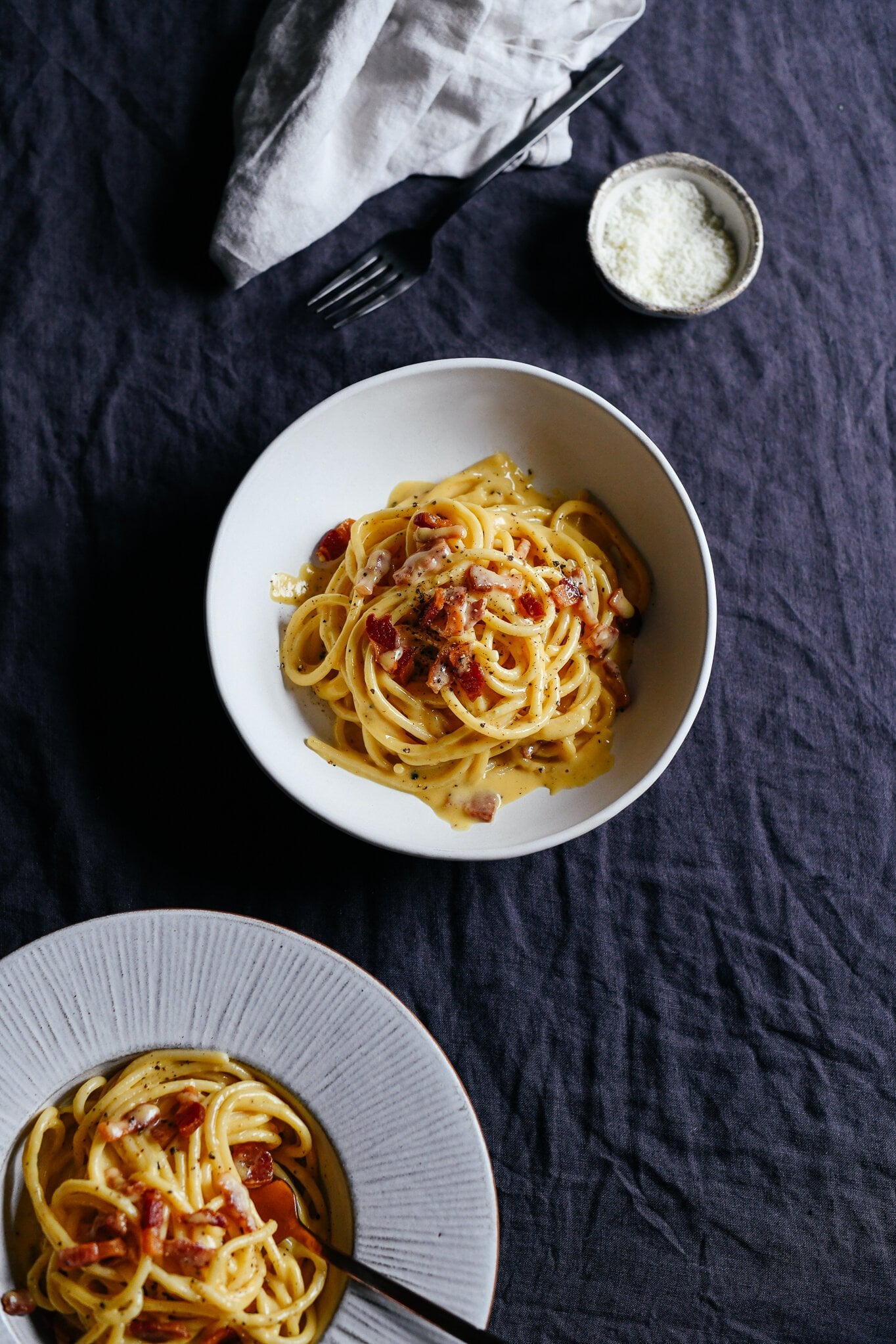 A bowl of spaghetti carbonara is shown from above. The sauce is creamy, glossy and deeply yellow, with crispy pieces of guanciale on top - just like a Roman-style carbonara is supposed to be.
