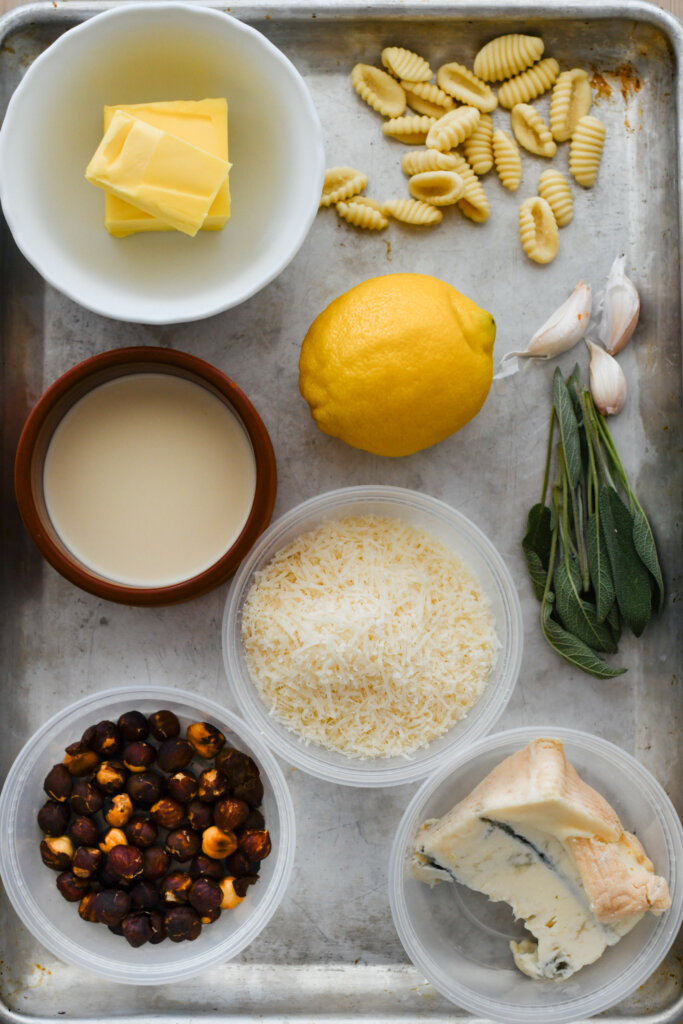 Flat lay of ingredients for cavatelli with gorgonzola and hazelnuts: pasta, butter, lemon, garlic, sage, cheese, cream, and toasted hazelnuts.