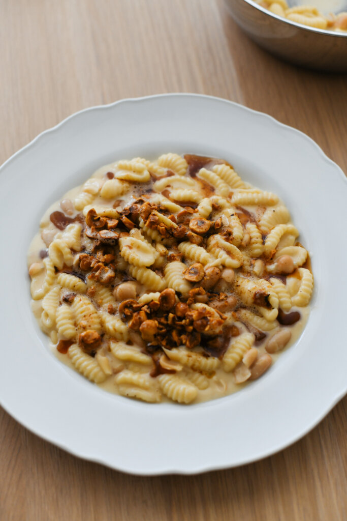 Cavatelli with gorgonzola sauce and white beans, served on a white bistro plate and topped with brown butter and roasted hazelnuts 
