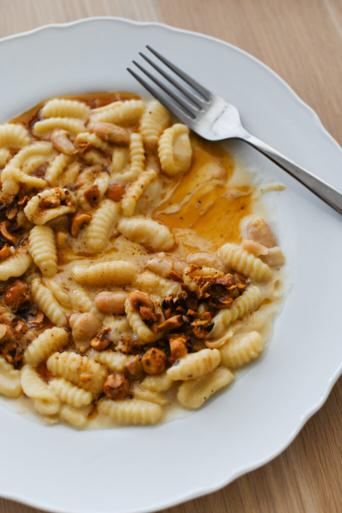 Creamy cavatelli with white beans and gorgonzola, topped with brown butter and toasted hazelnuts, served on a white plate with a fork.