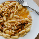A white bistro plate with partially eaten, handmade cavatelli pasta in a creamy gorgonzola and white bean sauce, topped with brown butter and roasted hazelnuts.
