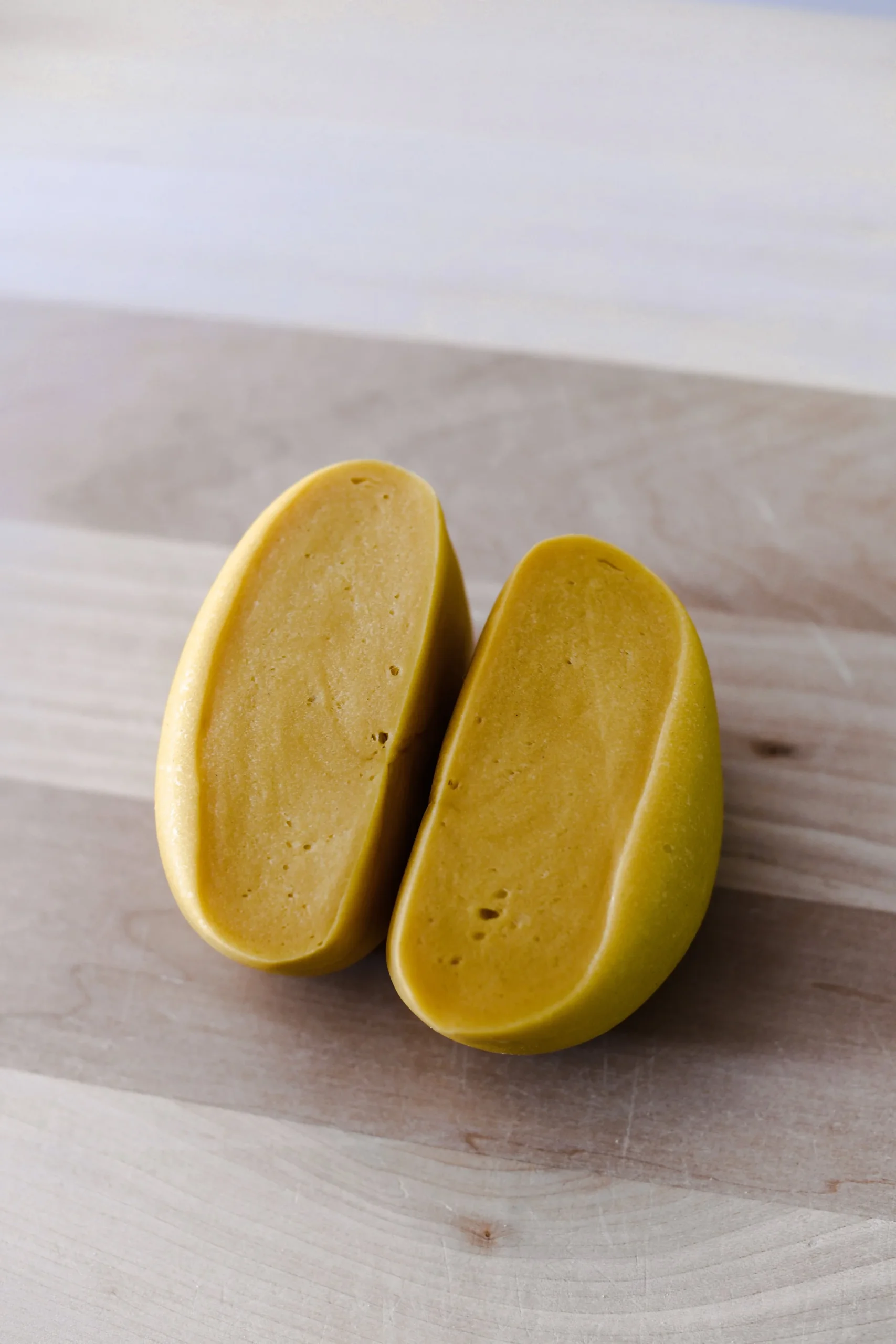 A cut section of a ball of fresh egg pasta dough shown resting on a wooden board. Visible air pockets and small holes are visible within the dough.