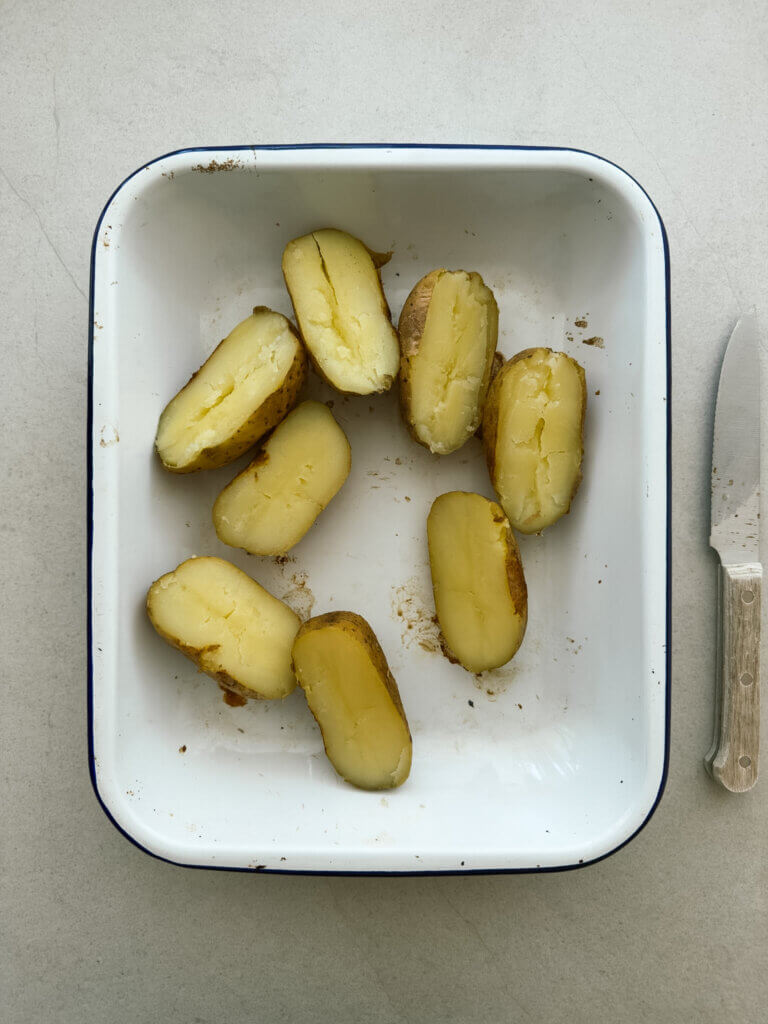 Roast désirée potatoes cut in half in a baking tray. 