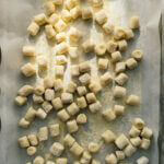 Fresh potato gnocchi sit on a baking sheet, dappled in sunlight.