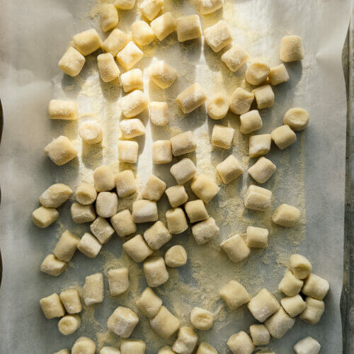 Fresh potato gnocchi sit on a baking sheet, dappled in sunlight.