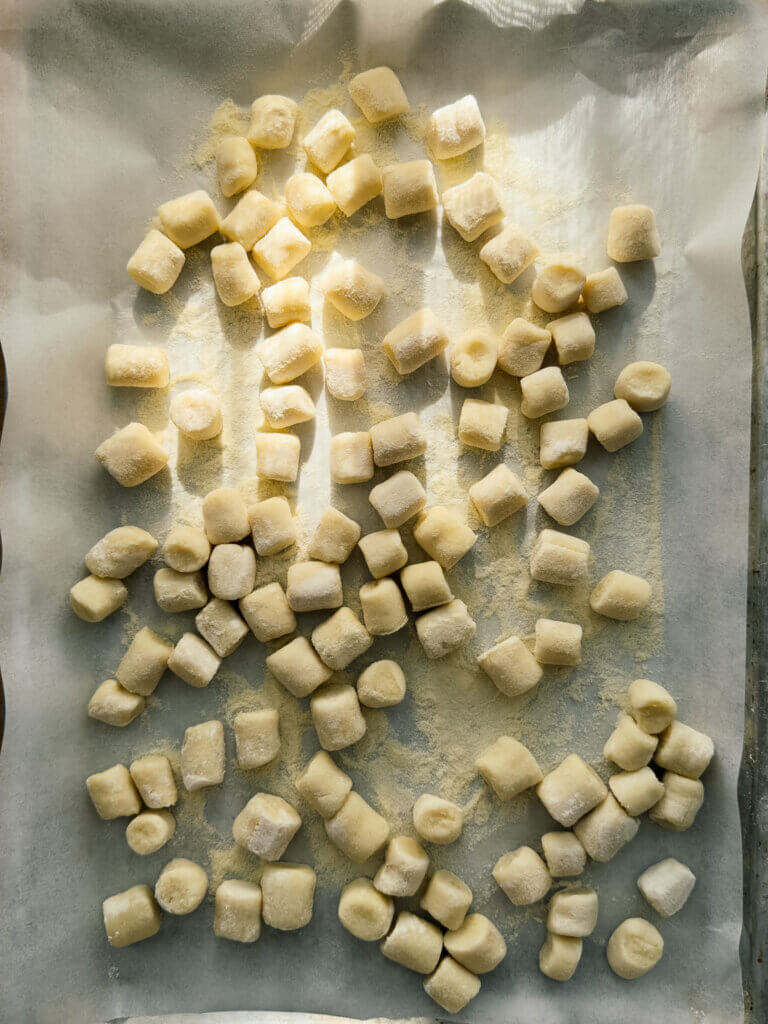 Fresh potato gnocchi sit on a baking sheet, dappled in sunlight. 