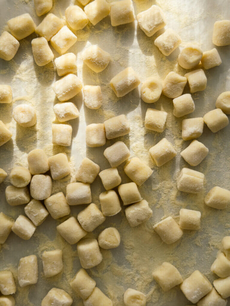 A baking sheet dappled in sunlight, with a layer of fresh potato gnocchi dusted in semolina flour.