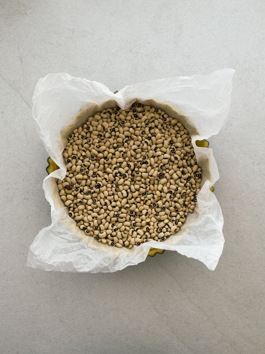 Dried black eyed beans fill a raw pastry shell lined with parchment paper, ready for blind baking.