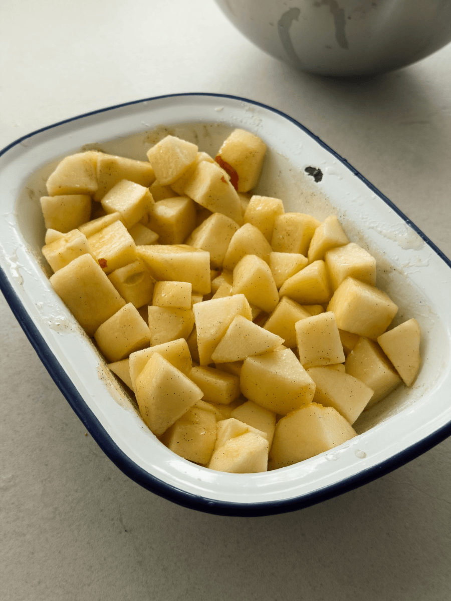 Peeled and cut apple pieces coated in vanilla bean paste, sugar and fresh lemon juice sit in a small Falcon enamel baking dish. 