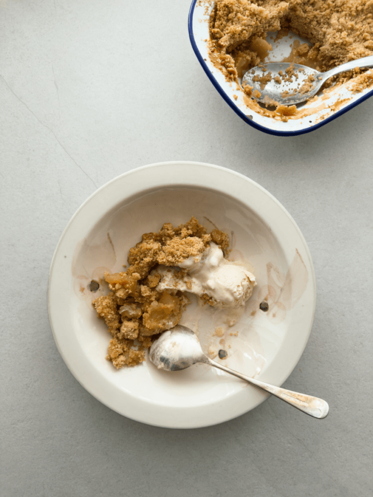 Apple crumble served in a vintage bowl is shown from above, with a scoop of ice cream.