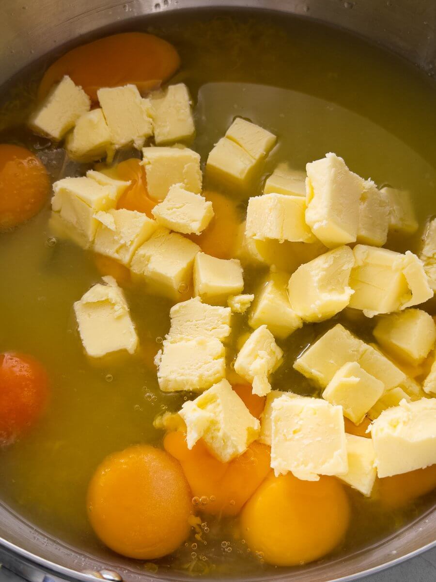Eggs, sugar, lemon juice and zest, and cubes of butter are combined in a stainless steel pan.