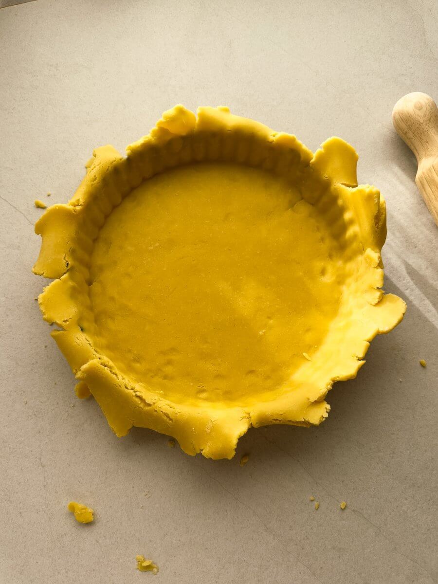 A top down photo of sweet pastry dough lining a fluted tart pan. The edges are rough and haven't been trimmed.