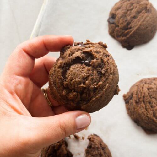 A hand holds a chunky chocolate tahini cookie, fresh out of the oven.