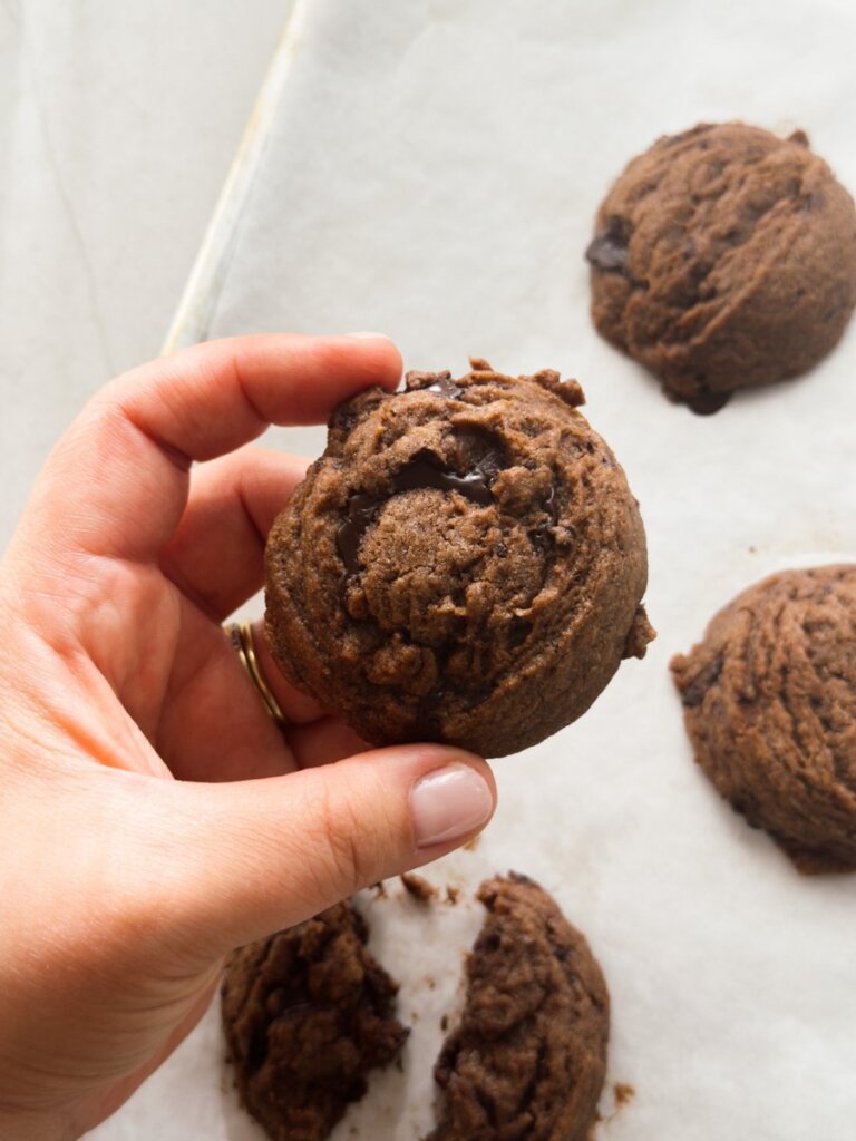 A hand holds a chunky chocolate tahini cookie, fresh out of the oven.