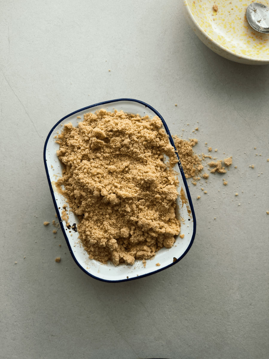 A top-down view of an apple crumble right before it's baked, showing a heaping mound of golden crumble topping, that spilling over the edge of the baking dish. 