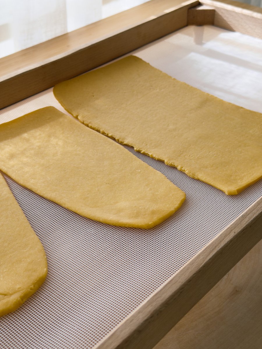 Sheets of fresh egg pasta dry on a mesh pasta drying tray.