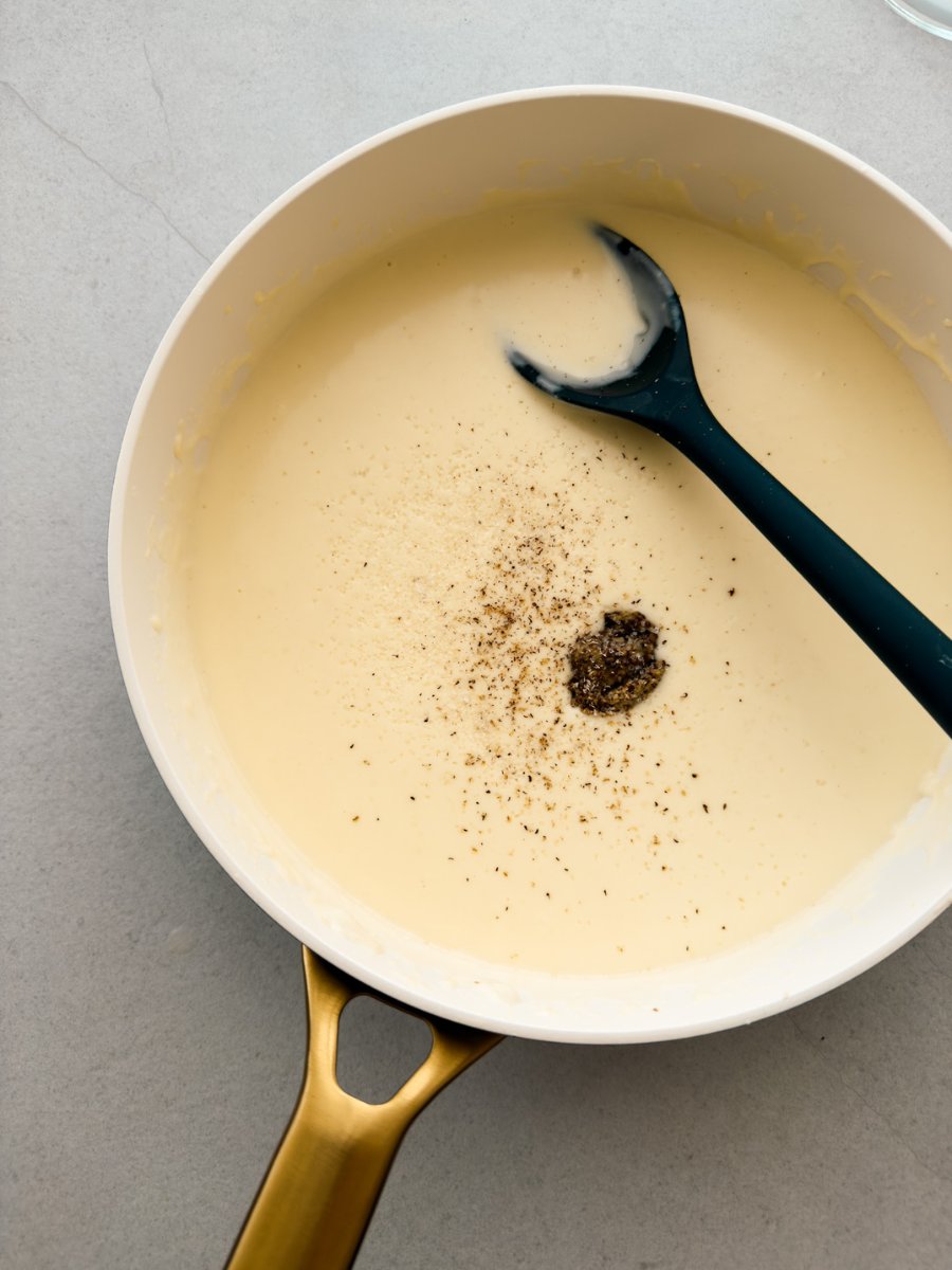 A pan containing béchamel sauce with a dollop of wholegrain mustard and grated nutmeg is shown from above. 