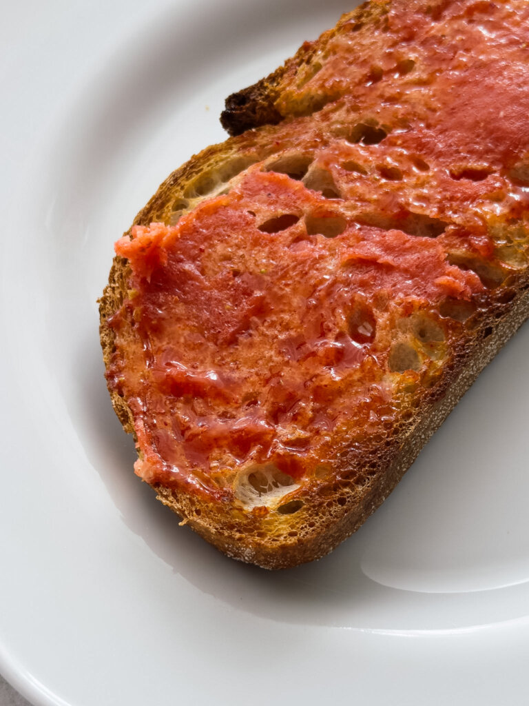 A close up shot of a slice of toasted sourdough slathered in a vibrant pink strawberry butter