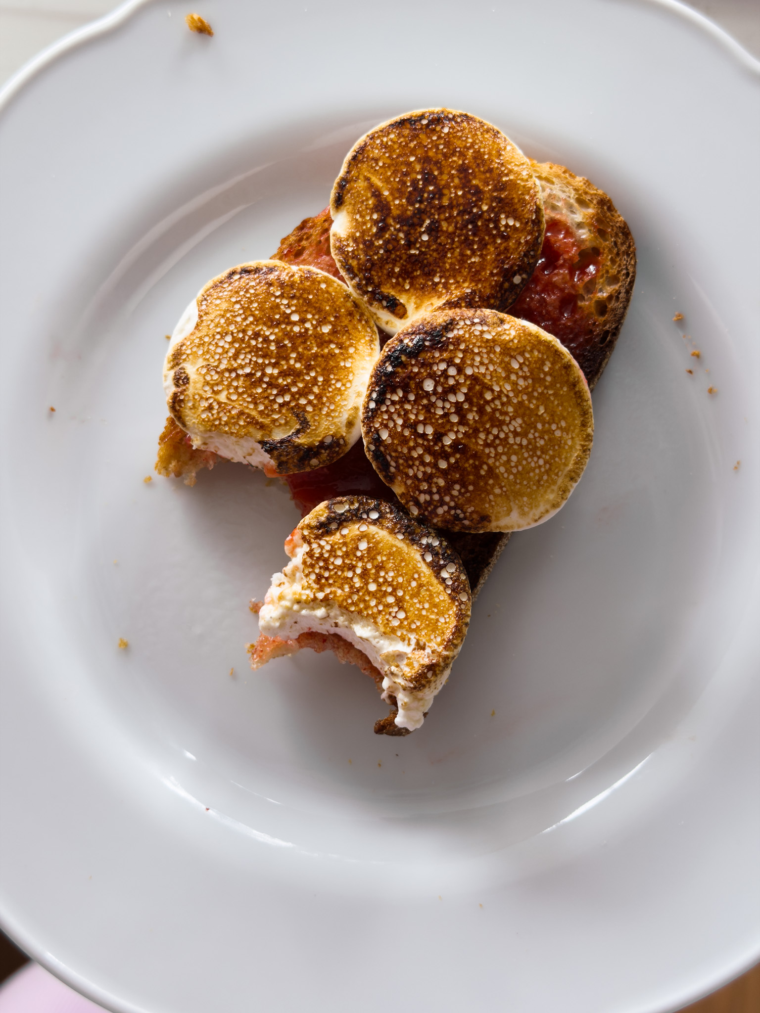 A top down photo of toast topped with toasted marshmallows and strawberry jam, with a couple of bites taken out of it.