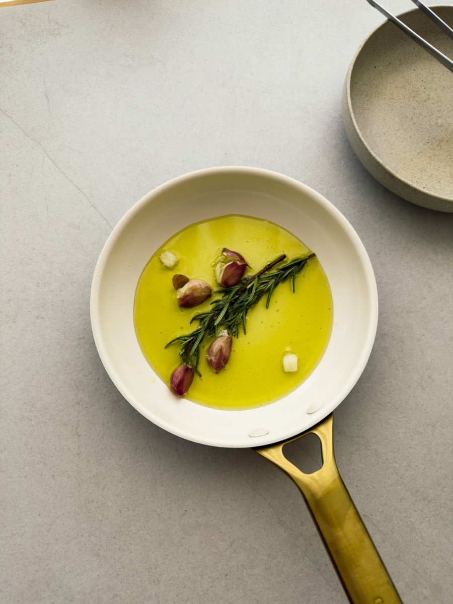 A top down photo of a small frying pan containing olive oil, garlic and rosemary that have been gently cooked to infuse the oil. 