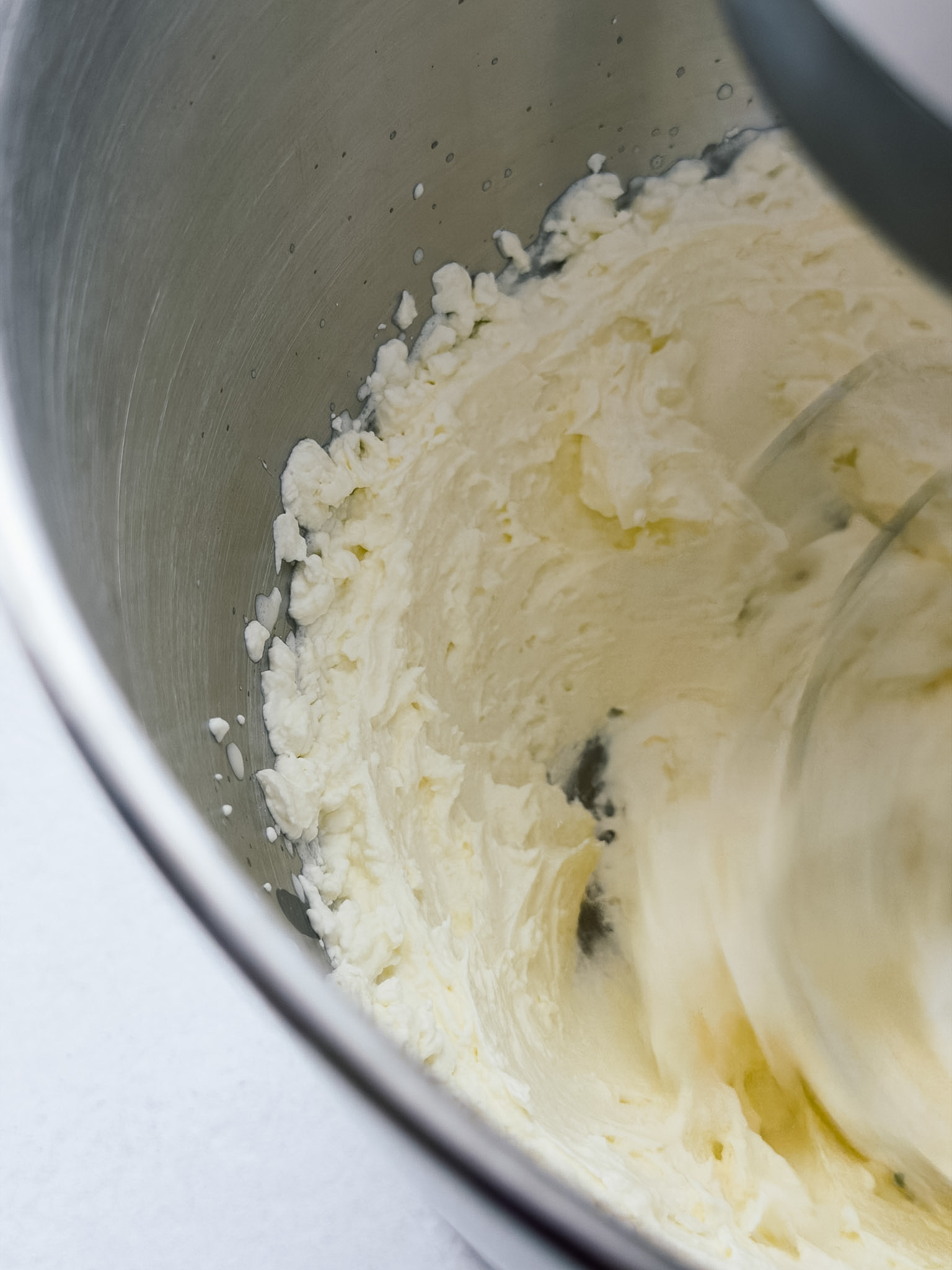 A close of photo of a stand mixer whipping cream for butter, the cream has thickened and starting to split.