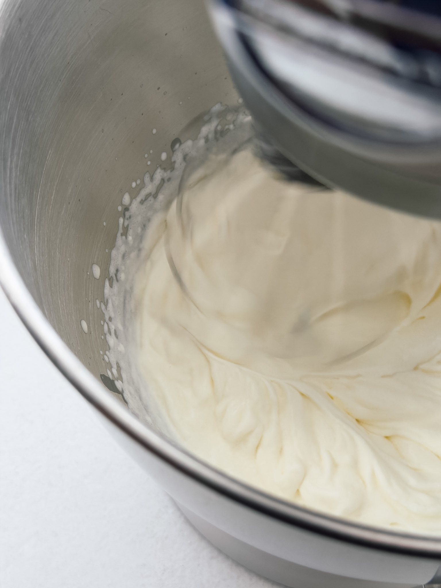 A close up photo of a stand mixer containing cream that's being whipped.