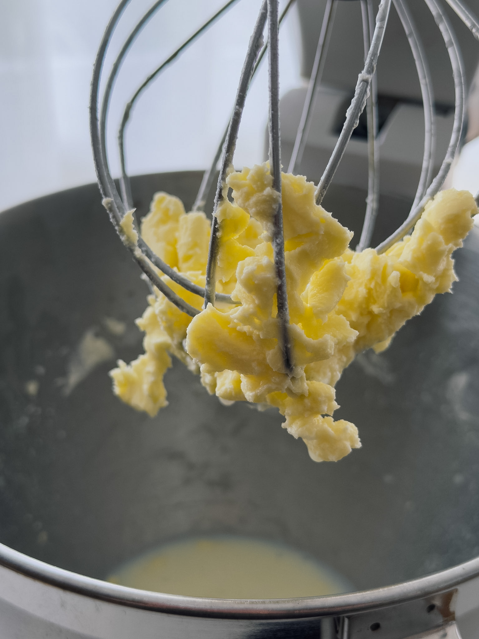 The whisk of a stand mixer covered in large clumps of freshly churned butter.