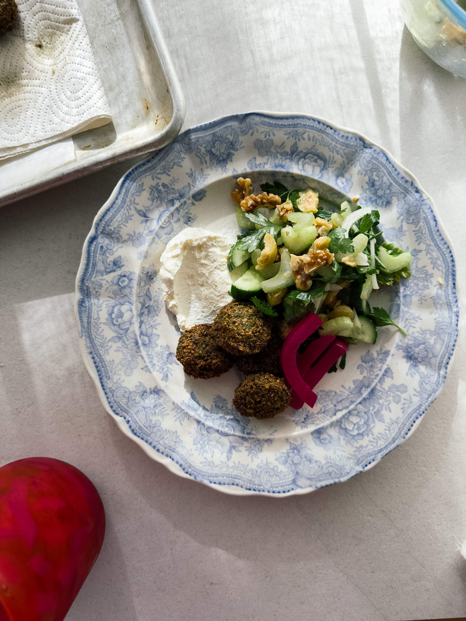 A top down photo of a blue patterned plate with a few falafel on it, alongside a herby green salad, pickled Lebanese turnips, and fresh labneh. 