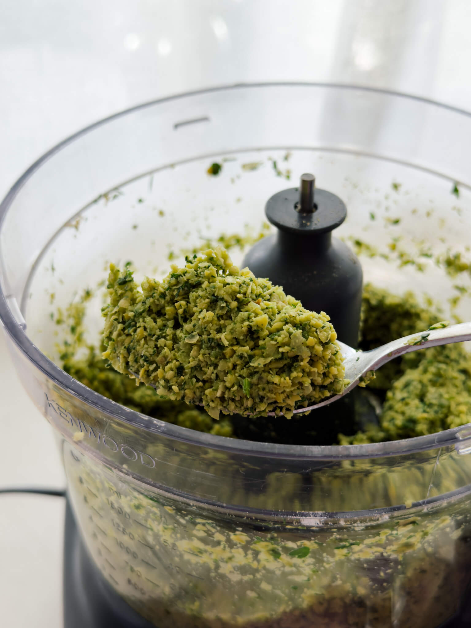 A spoon holds a heap of freshly blended falafel mixture straight from a food processor. 