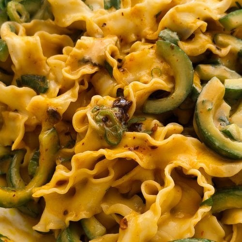 A close up photo of Taiwanese-style knife cut noodles, served in a creamy peanut sauce, with cucumbers, spring onions, coriander and chilli crisp oil.