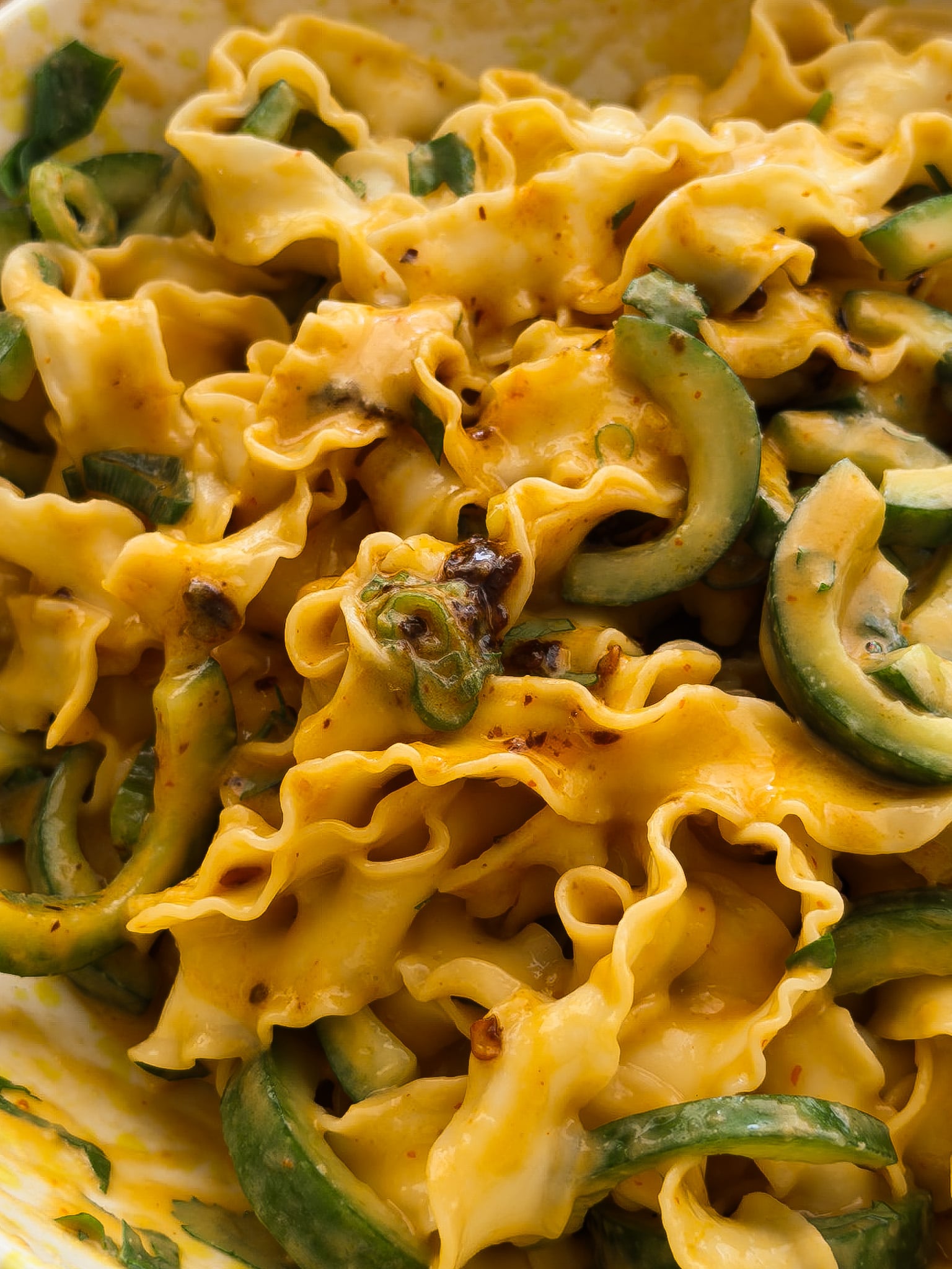 A close up photo of Taiwanese-style knife cut noodles, served in a creamy peanut sauce, with cucumbers, spring onions, coriander and chilli crisp oil. 