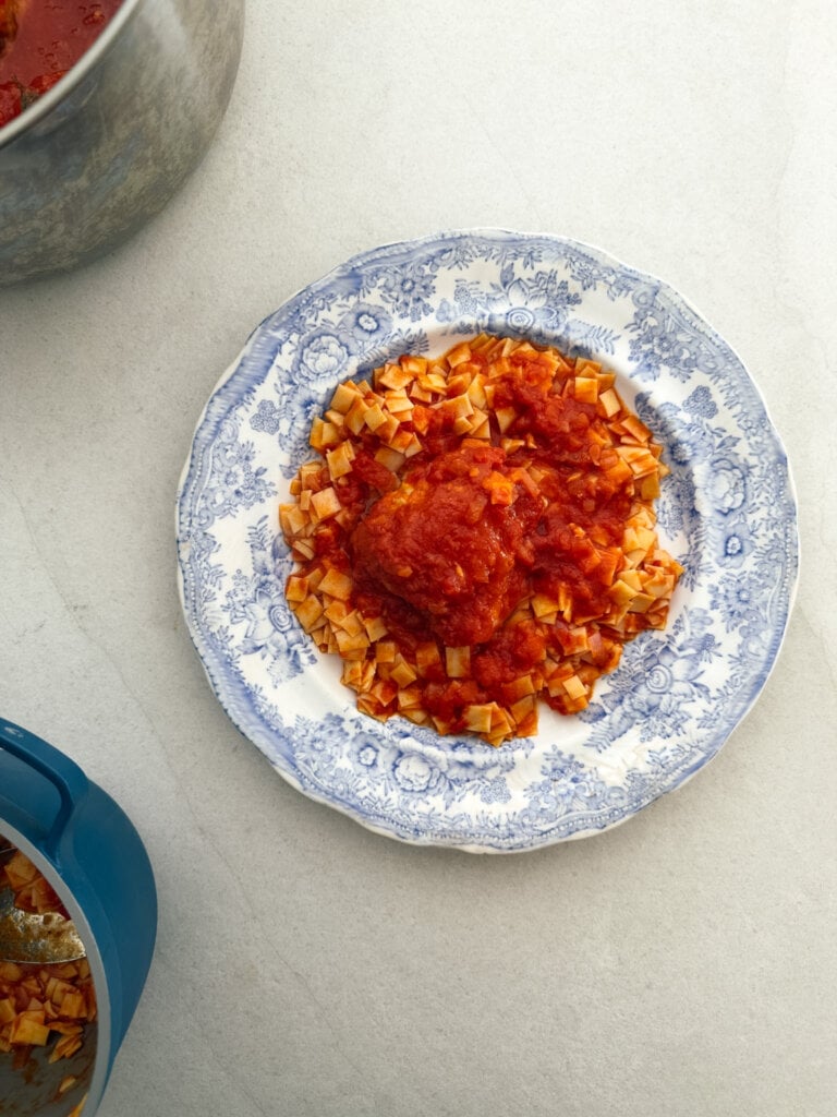 A top down photo of a plate of Greek chicken in tomato sauce, served with traditional hilopites pasta.