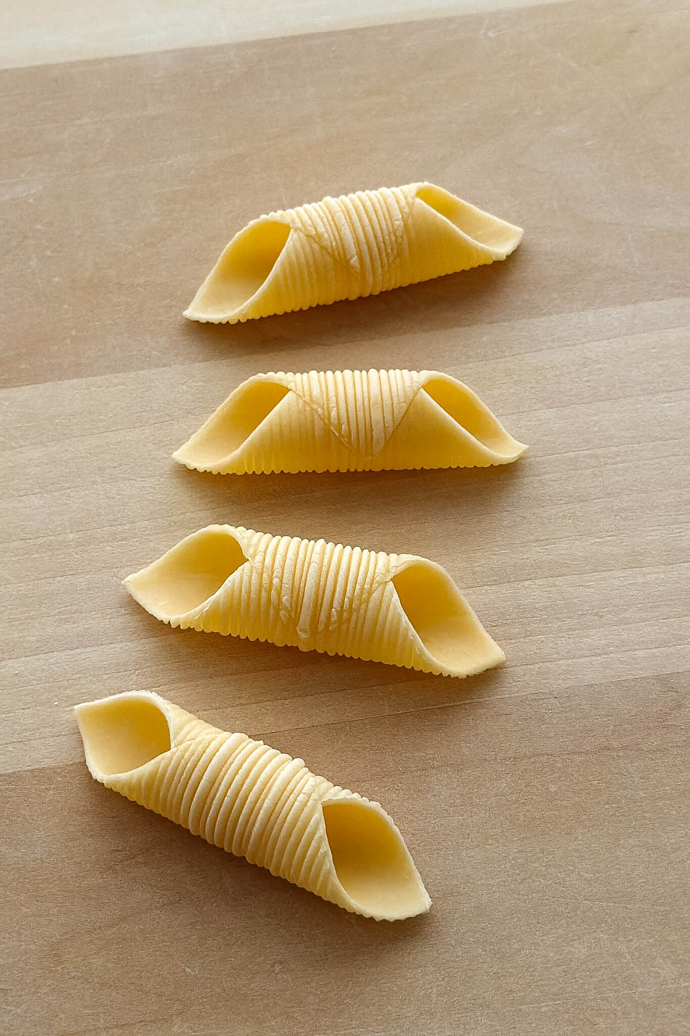 A close up photo of 4 pieces of homemade garganelli pasta, a short tubular pasta with a ridged exterior and pointed ends.
